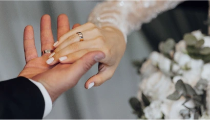 Two hands intertwined, one in a dark suit jacket and the other in a long-sleeved white dress