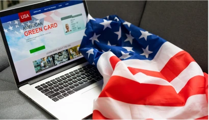 A laptop displaying a page for the American Green Card with an American flag draped over the keyboard