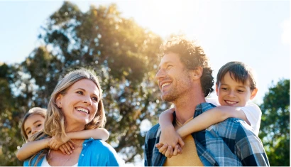 A family of four enjoying a sunny day outdoors, the two children riding on their parents’ backs